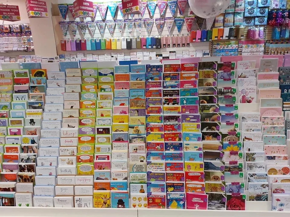 A wall of greeting cards under header signs reading New Home, Thank You, Blank, Good Luck, Congratulations, Leaving, Birth and Christening