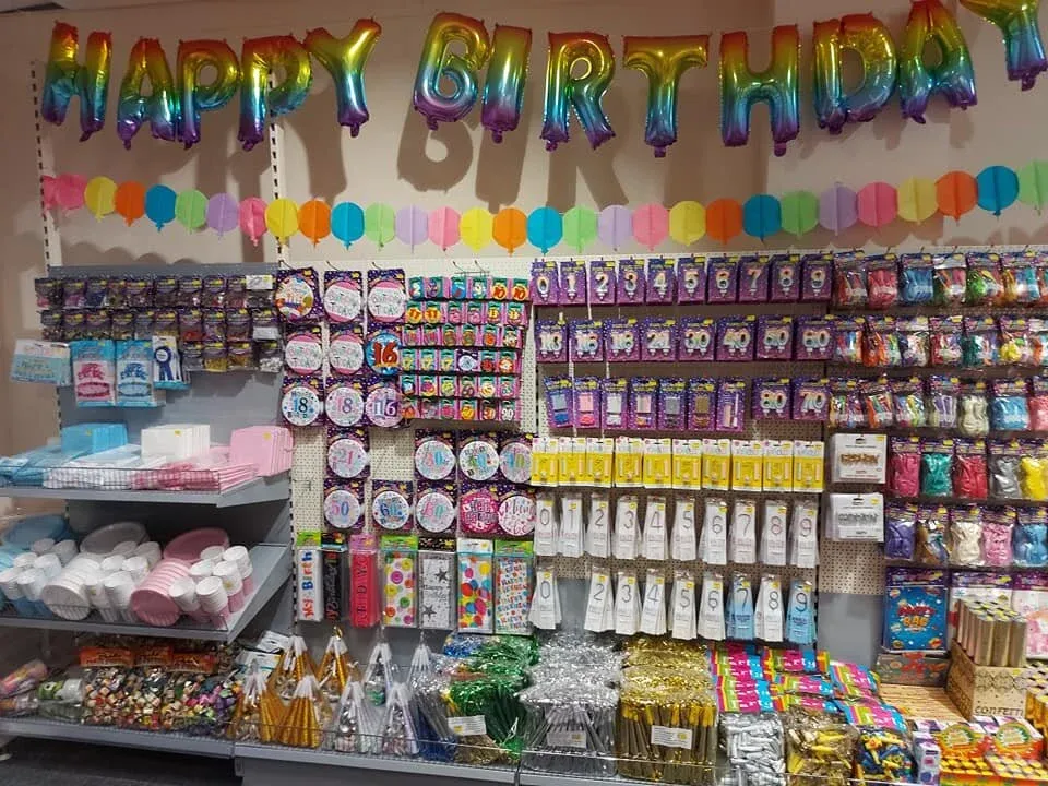 A wall of foil letter balloons spelling Happy Birthday, over shelves of party goods
