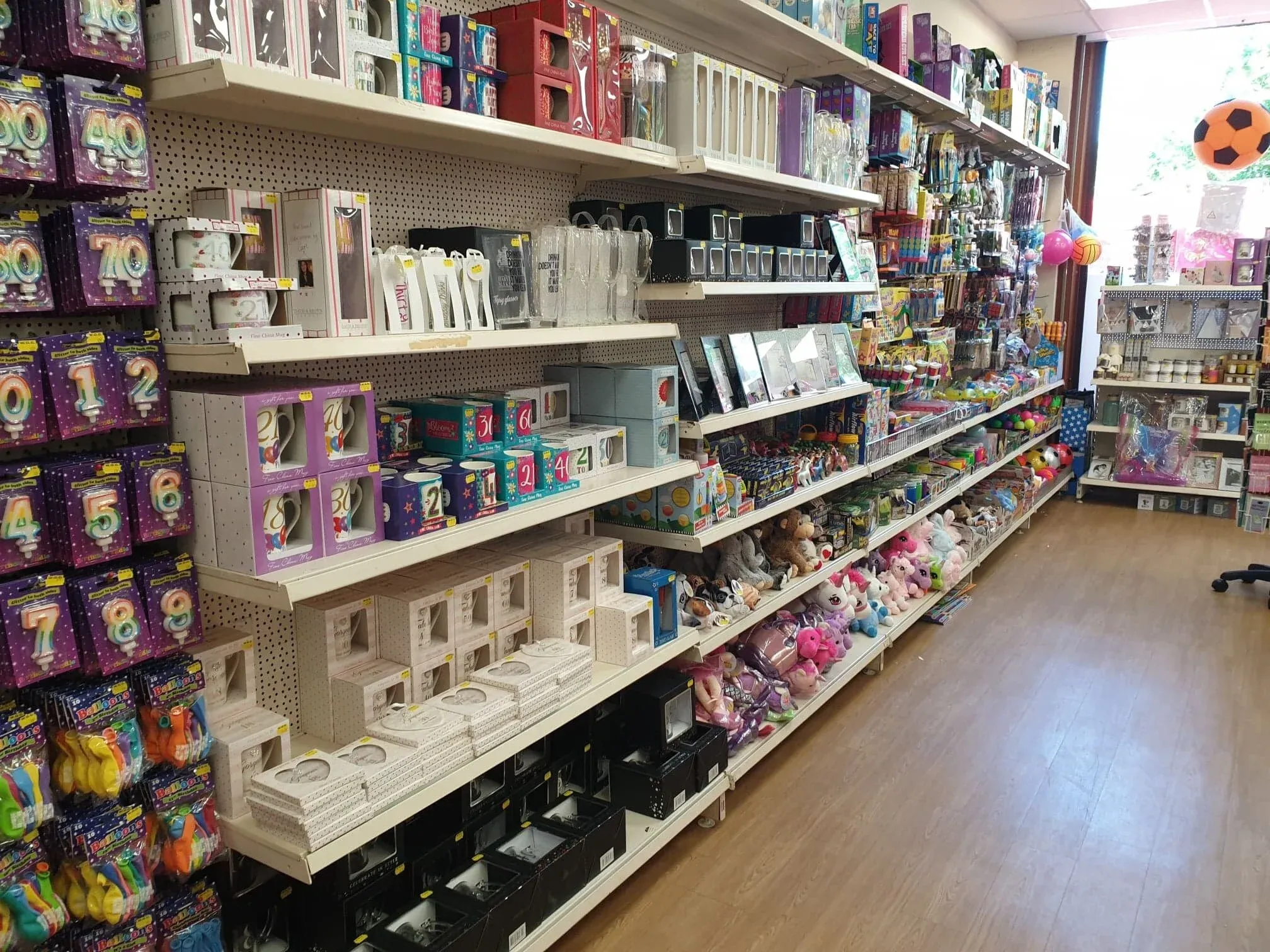 Inside a G&T's World of Cards shop: an aisle of number candles, balloons, mugs and soft toys, with daylight at the far end